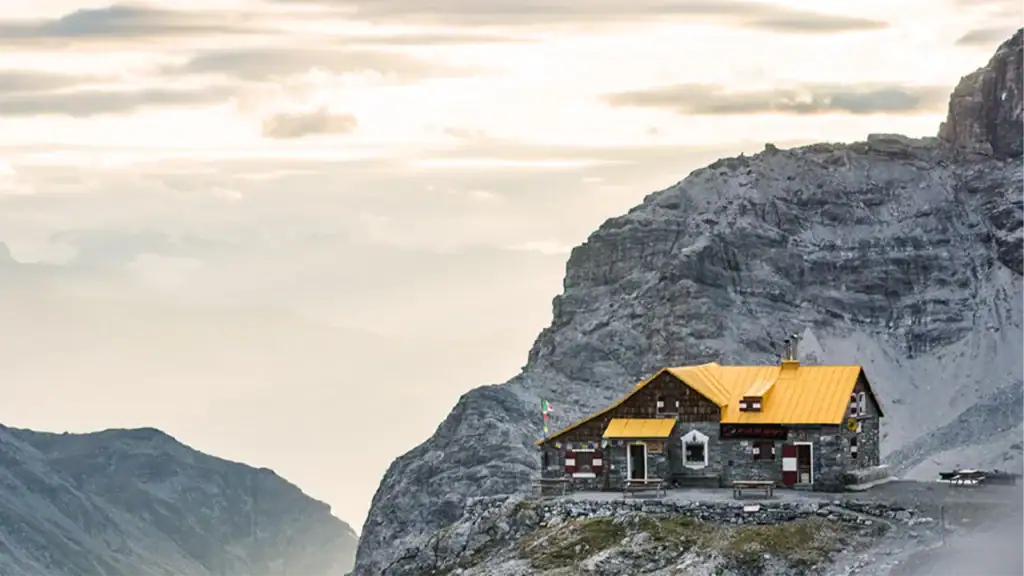 Casa di montagna in pietra con tetto giallo in un paesaggio alpino montuoso.