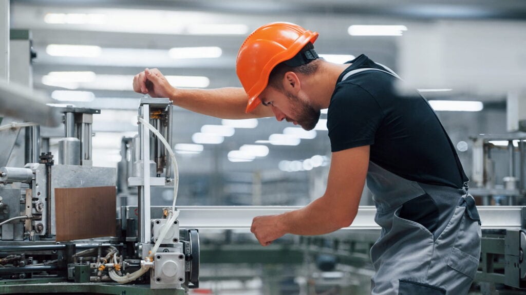 Operaio in fabbrica con casco controlla macchinari TNT produzione.
